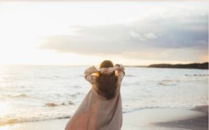 a woman feeling calm and refreshed looking out over the ocean
